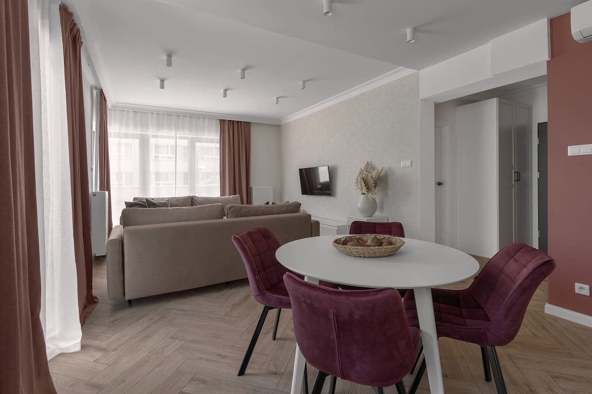 A modern living room with a sofa, a dining table with chairs, and a TV mounted on the wall.