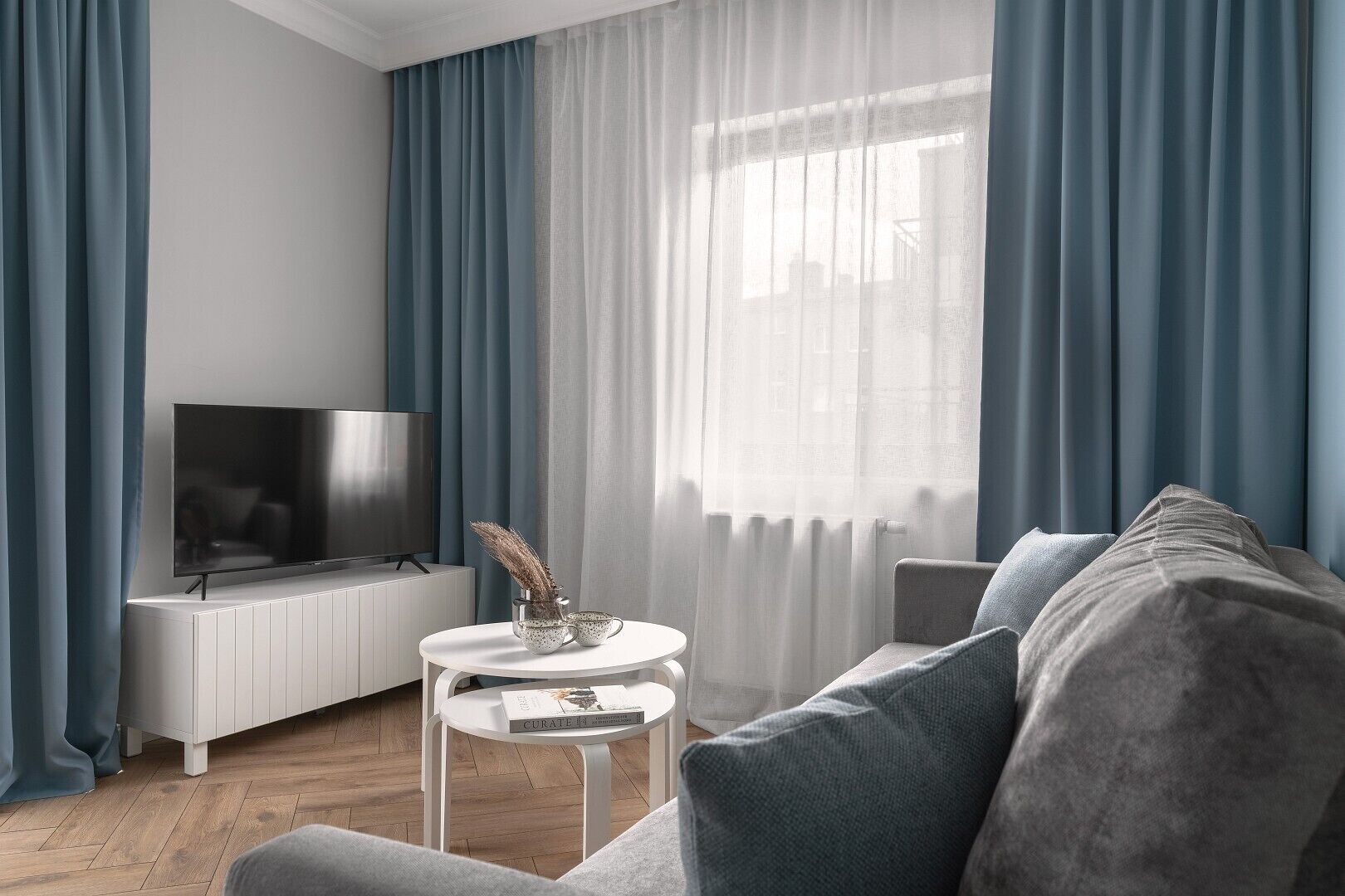 A modern living room with a flat-screen TV, a white sideboard, a round coffee table with a book, and a grey sofa.