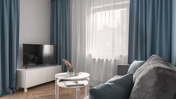 A modern living room with a flat-screen TV, a white sideboard, a round coffee table with a book, and a grey sofa.