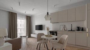 Una sala de estar moderna con un sofá, una mesa de comedor con sillas, un televisor montado en la pared y una zona de cocina con armarios y electrodomésticos.