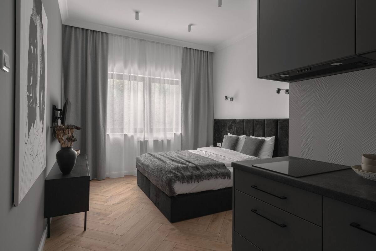 A modern bedroom with a bed, bedside tables, a dresser, and a large window with sheer curtains.