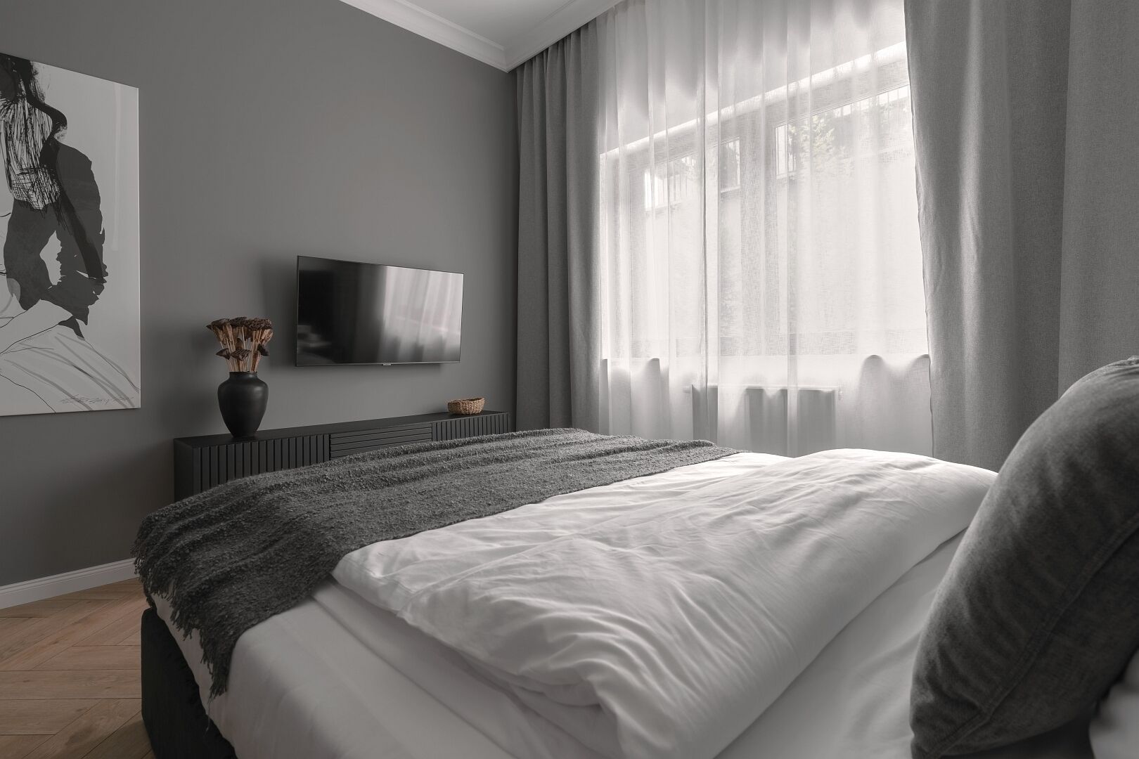 Un dormitori modern amb un llit gran, una televisió de pantalla plana a la paret i una finestra amb cortines de tul.
