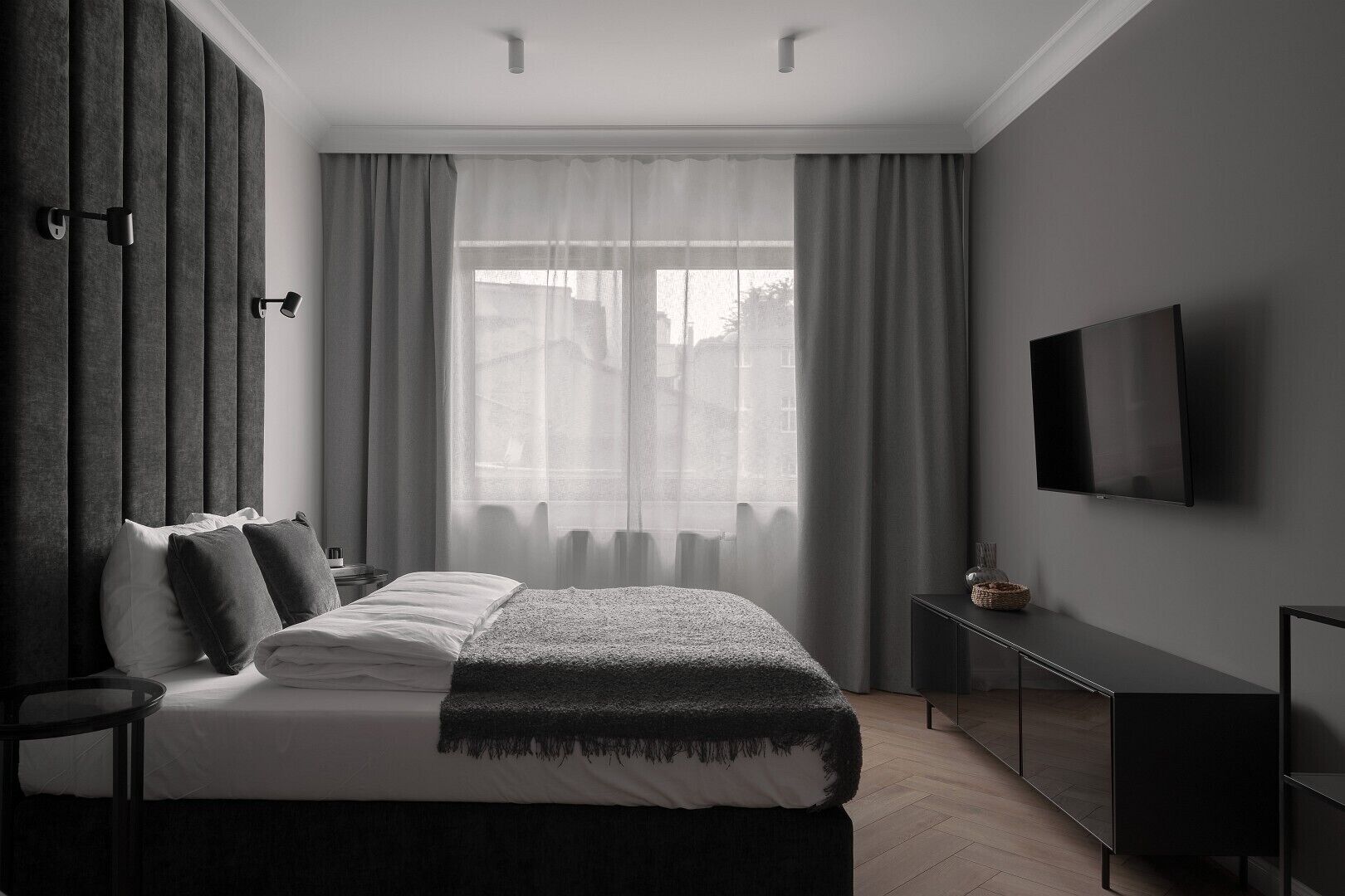 Un dormitorio moderno con cama, televisión y ventana con cortinas.