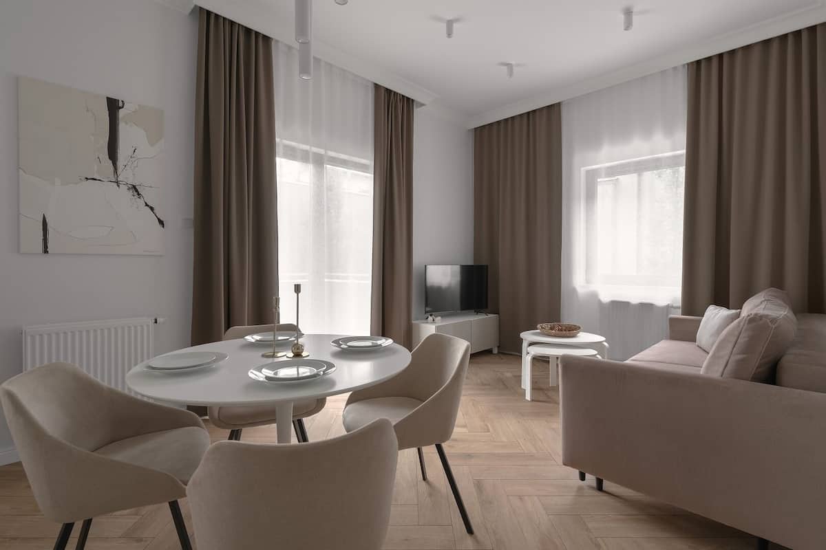 A modern living room with a round dining table, beige sofas, and a flat-screen TV.