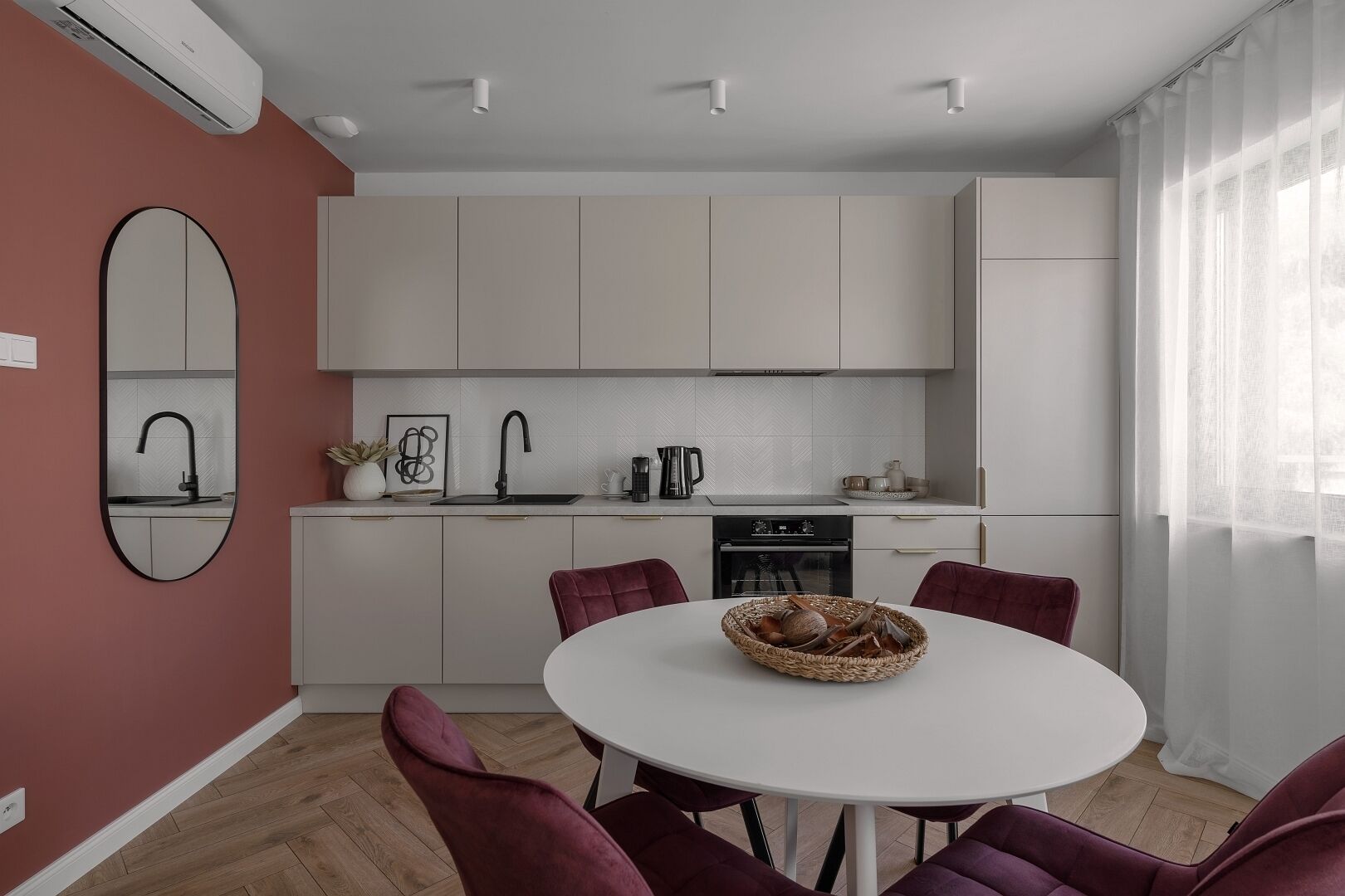 A modern kitchen with white cabinets, a round dining table with purple chairs, and a large mirror on the wall.