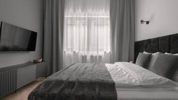 A modern bedroom with a large bed, a TV mounted on the wall, and a window with sheer curtains.