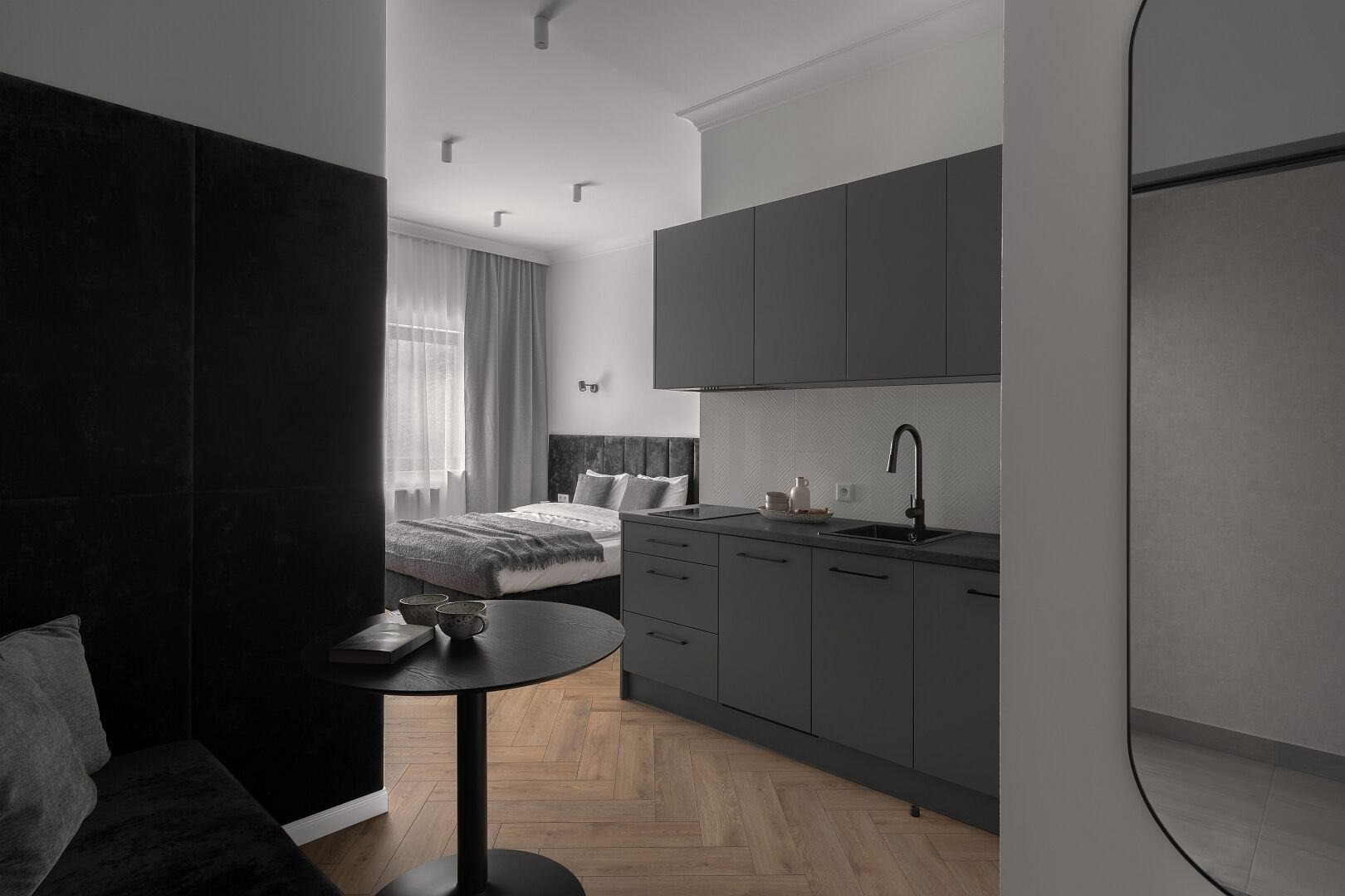 Moderni ja kompakti hotellihuone, jossa on pieni keittiönurkkaus, sängynpääty, pieni pyöreä pöytä ja sohva.