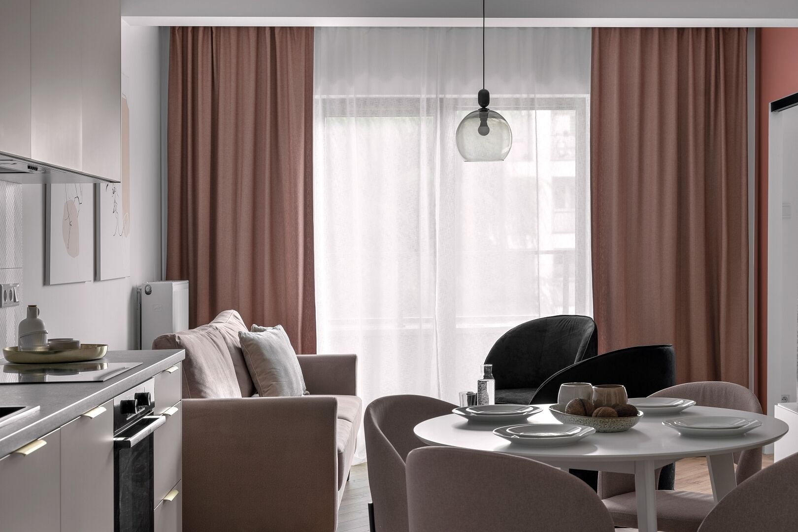 A modern kitchen with a dining area, featuring a round table, chairs, and a hanging light fixture.