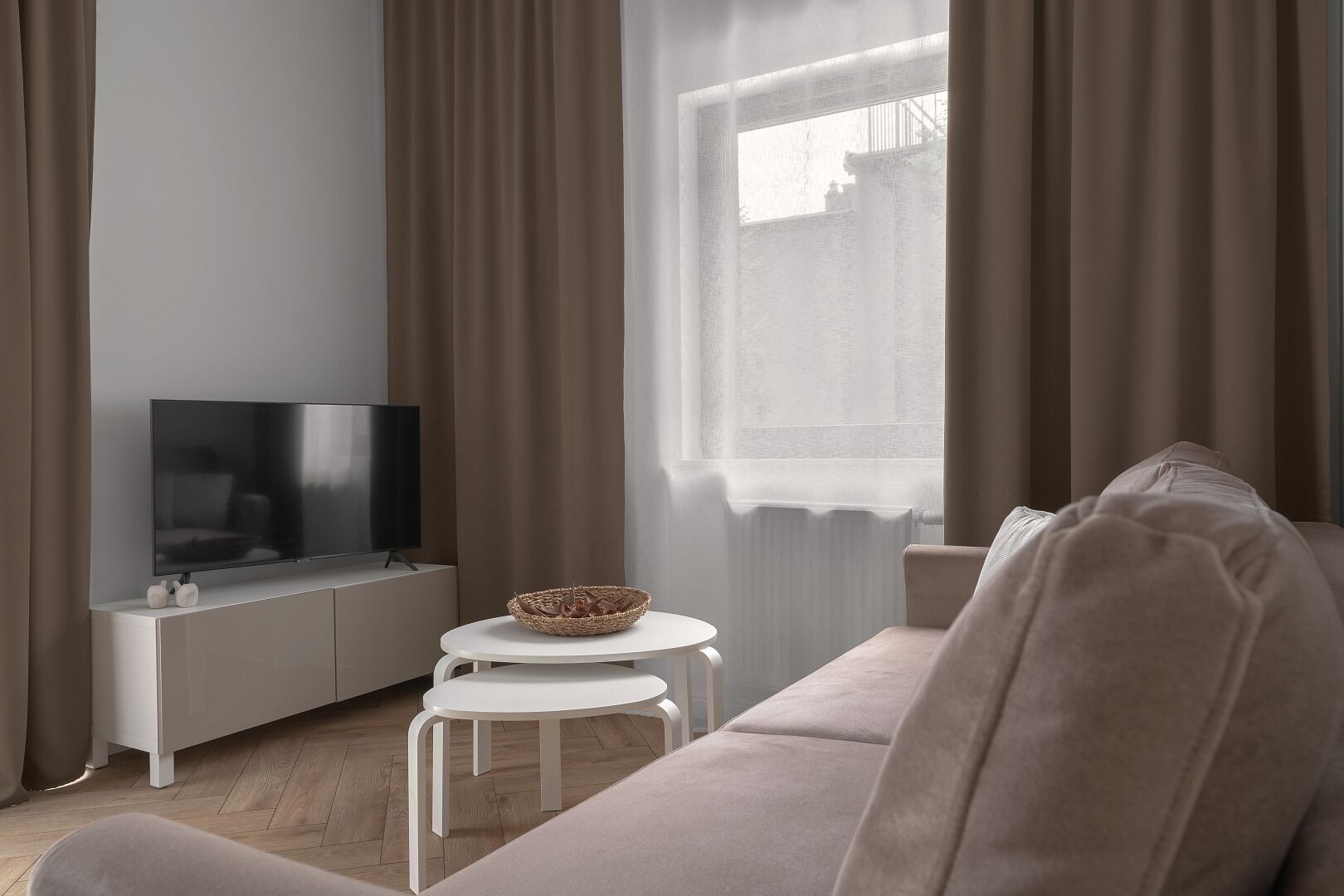Una sala de estar moderna con un televisor de pantalla plana, una consola blanca, una mesa redonda blanca, un sofá beige y una ventana con cortinas traslúcidas.