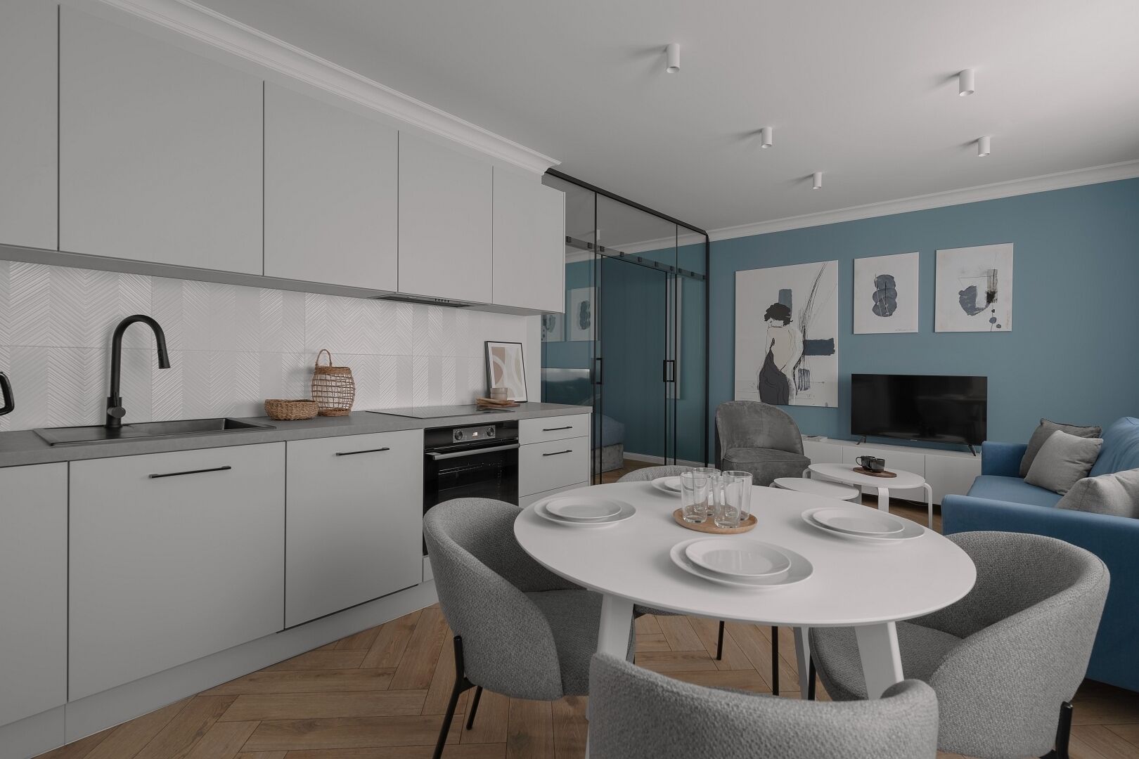 Una cocina moderna con armarios blancos, un grifo negro y una zona de comedor con una mesa blanca y sillas grises.