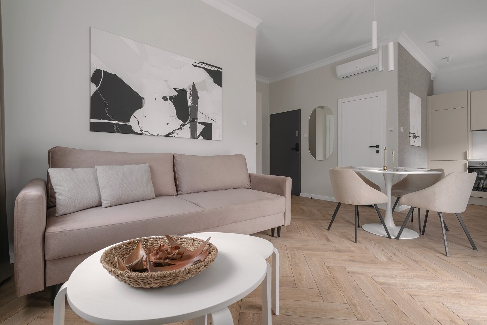 Una sala de estar moderna con un sofá color beige, una mesa redonda blanca y una cesta tejida.