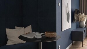 Una sala de estar moderna con una pared de acento azul oscuro, una mesa redonda negra y un sofá azul oscuro con cojines blancos.