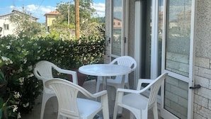 Un balcon avec une table ronde et quatre chaises, une porte-fenêtre coulissante et une vue sur des immeubles et des arbres.