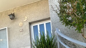 Un escalier en pierre menant à une porte dotée d’une fenêtre, un pot de fleurs placé sur les marches et une rambarde métallique sur le côté droit.