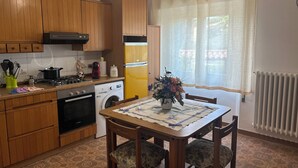 Une cuisine compacte avec des meubles en bois, un lave-linge, un réfrigérateur jaune et une table à manger avec des chaises.