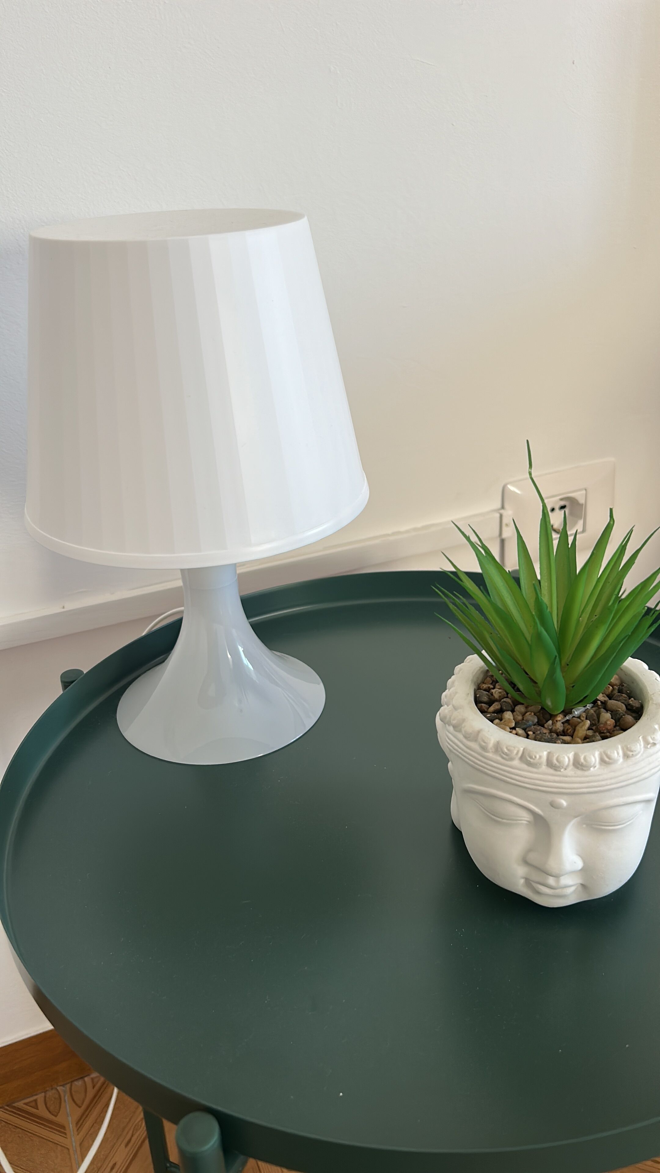 Una lámpara de mesa blanca sobre una mesa verde con una planta en maceta.