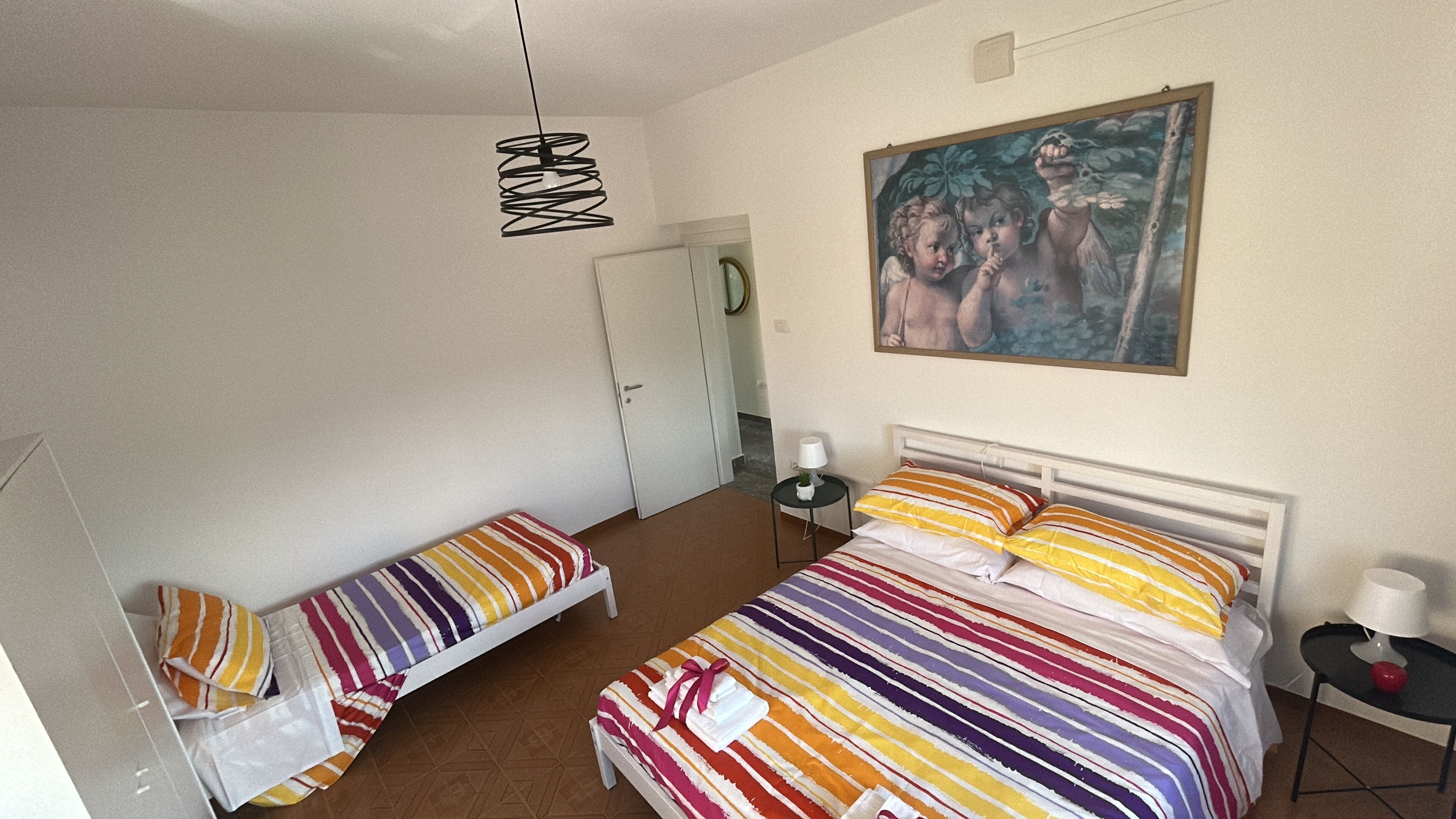 Ein Schlafzimmer mit einem Bett, einem Nachttisch, einer Lampe, einem Bild an der Wand und einer Tür.