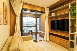A modern living room with a sofa, a television, and a balcony with a city view.
