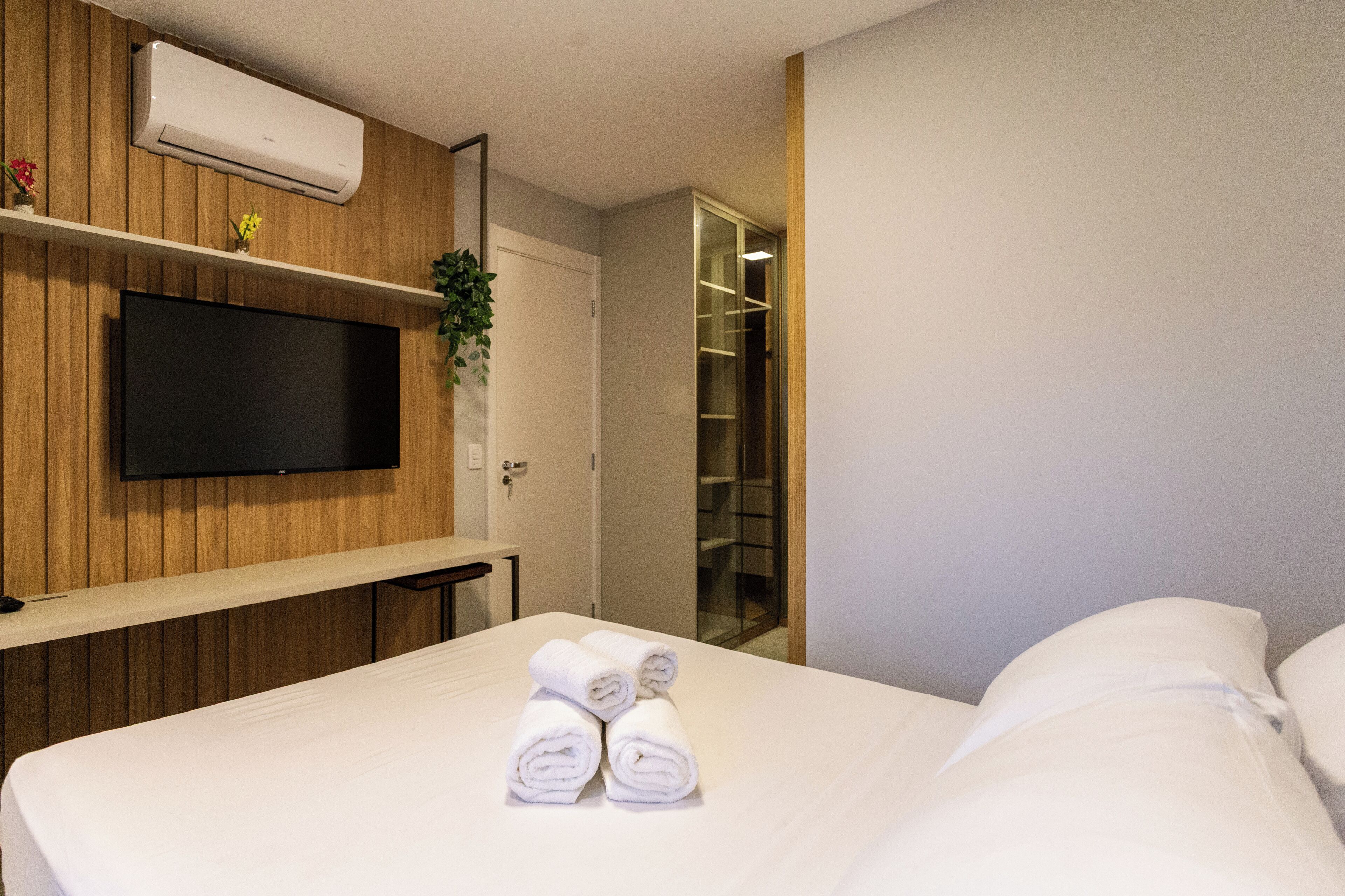 A hotel room with a bed, a flat-screen TV mounted on a wooden panel wall, a mirror, and a walk-in closet.