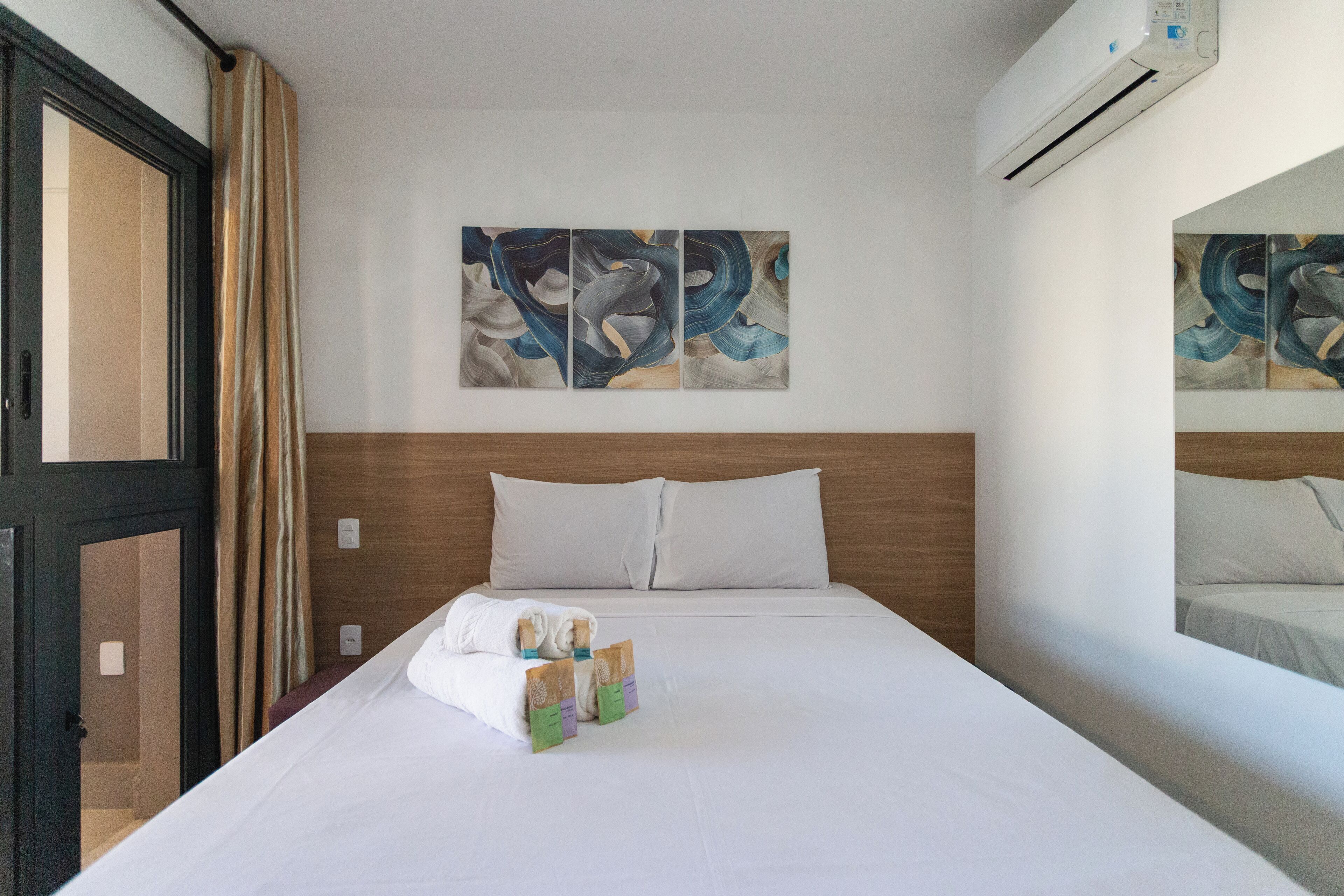 Une chambre d’hôtel avec un lit, des oreillers, une fenêtre avec des rideaux et des œuvres d’art mural.