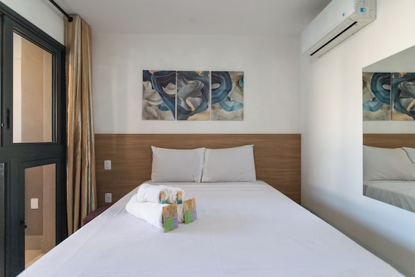 A hotel room with a bed, pillows, a window with curtains, and wall art.