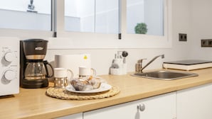 A kitchen with a coffee maker, cups, a plate with pastries, a sink, and a window with a view of a building.