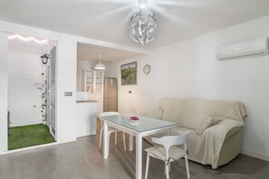 A modern living space with a glass dining table, white chairs, a beige sofa, a small kitchen area, and a decorative globe light.