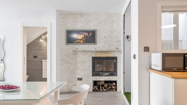 A modern kitchen with a stone fireplace, a flat-screen TV above it, and a dining area with a glass table and chairs.