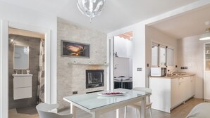 A modern kitchen with a fireplace, a dining area with a glass table, and a white cabinet.