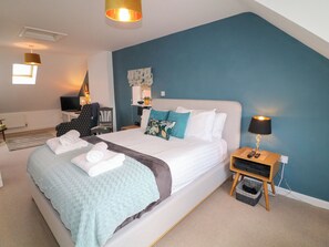A modern bedroom with a large bed, a bedside table with a lamp, a TV, and a small seating area with a chair and a table. - No 39 (Ashbourne)