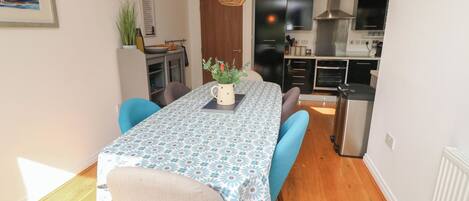 Une cuisine compacte dotée d’appareils électroménagers modernes, un coin repas avec une table et des chaises, et un luminaire suspendu.