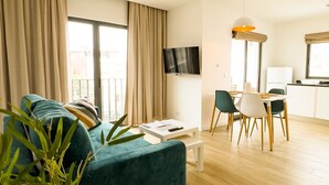 A modern living room with a teal sofa, a dining area with a white table and chairs, and a kitchen area with a refrigerator and a TV mounted on the wall. - BIA D'Olaf Apartments (Santa Maria)