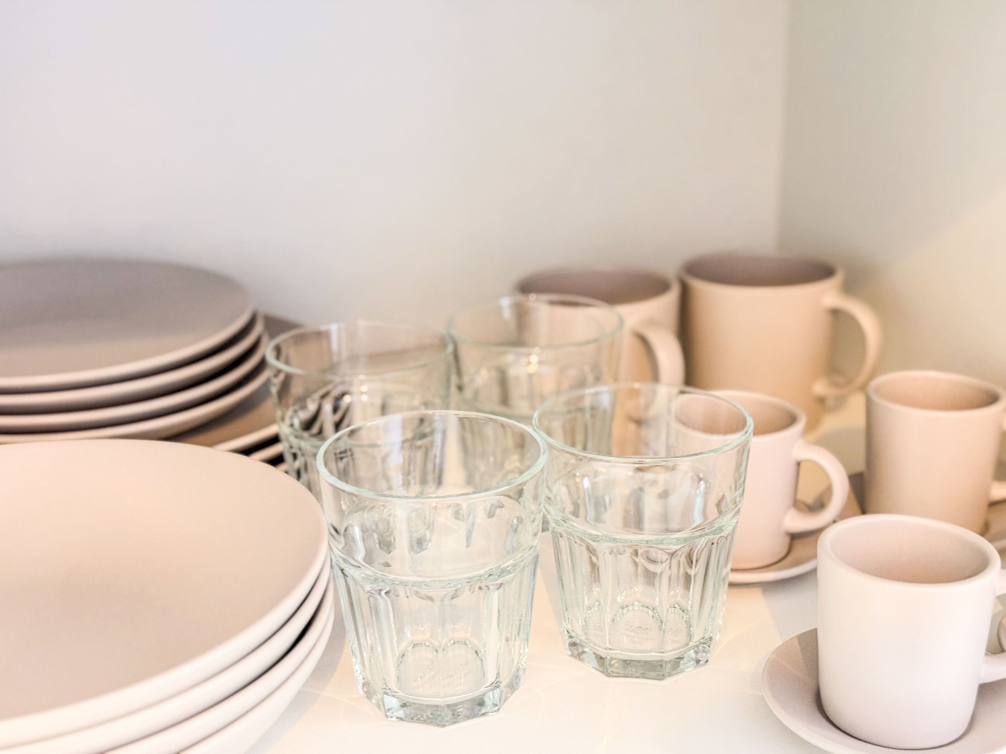 A table set with clear glass cups, plates, and mugs, arranged neatly.