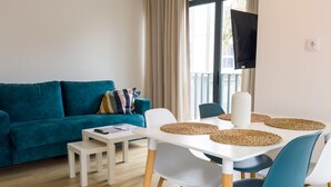 A modern living room with a teal sofa, a white dining table with blue chairs, and a large window with curtains. - BIA D'Olaf Apartments (Santa Maria)