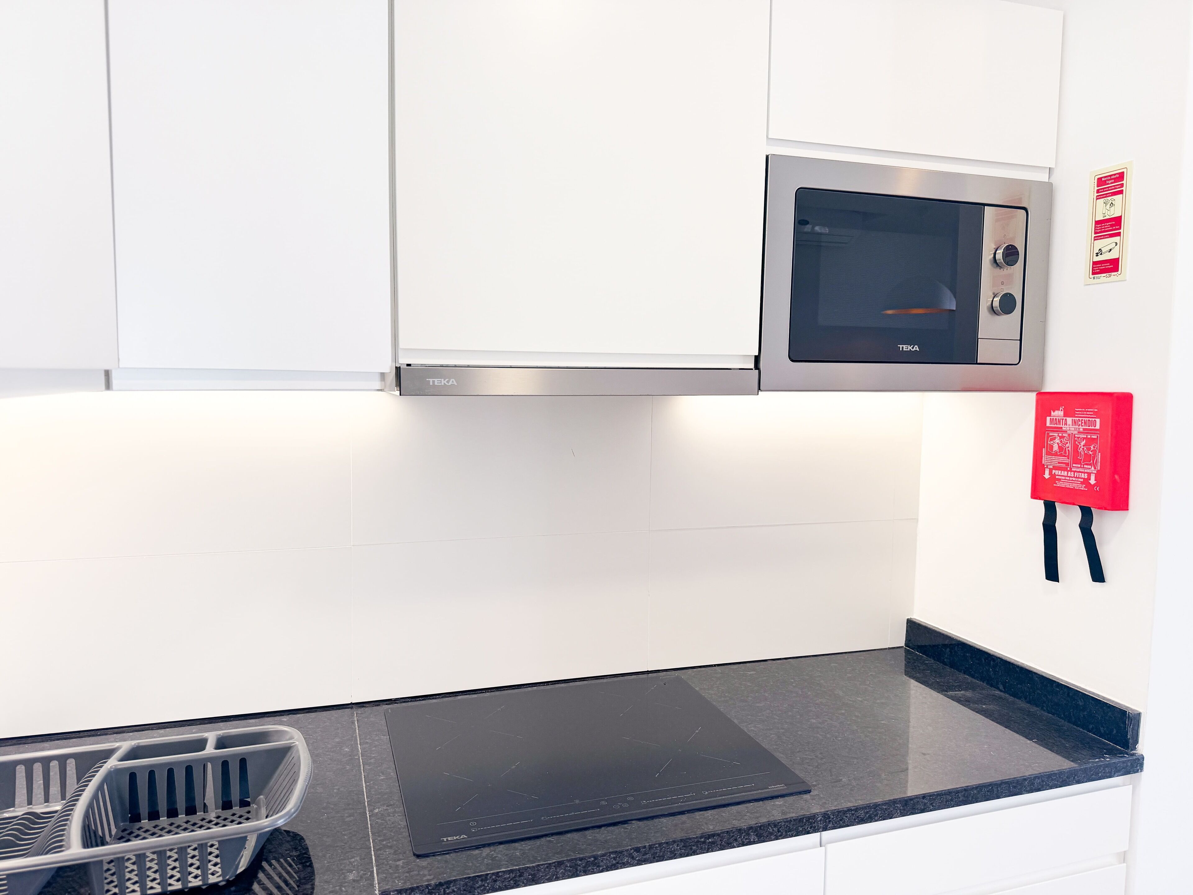 A kitchen with white cabinets, a black countertop, a microwave, and a red fire extinguisher.