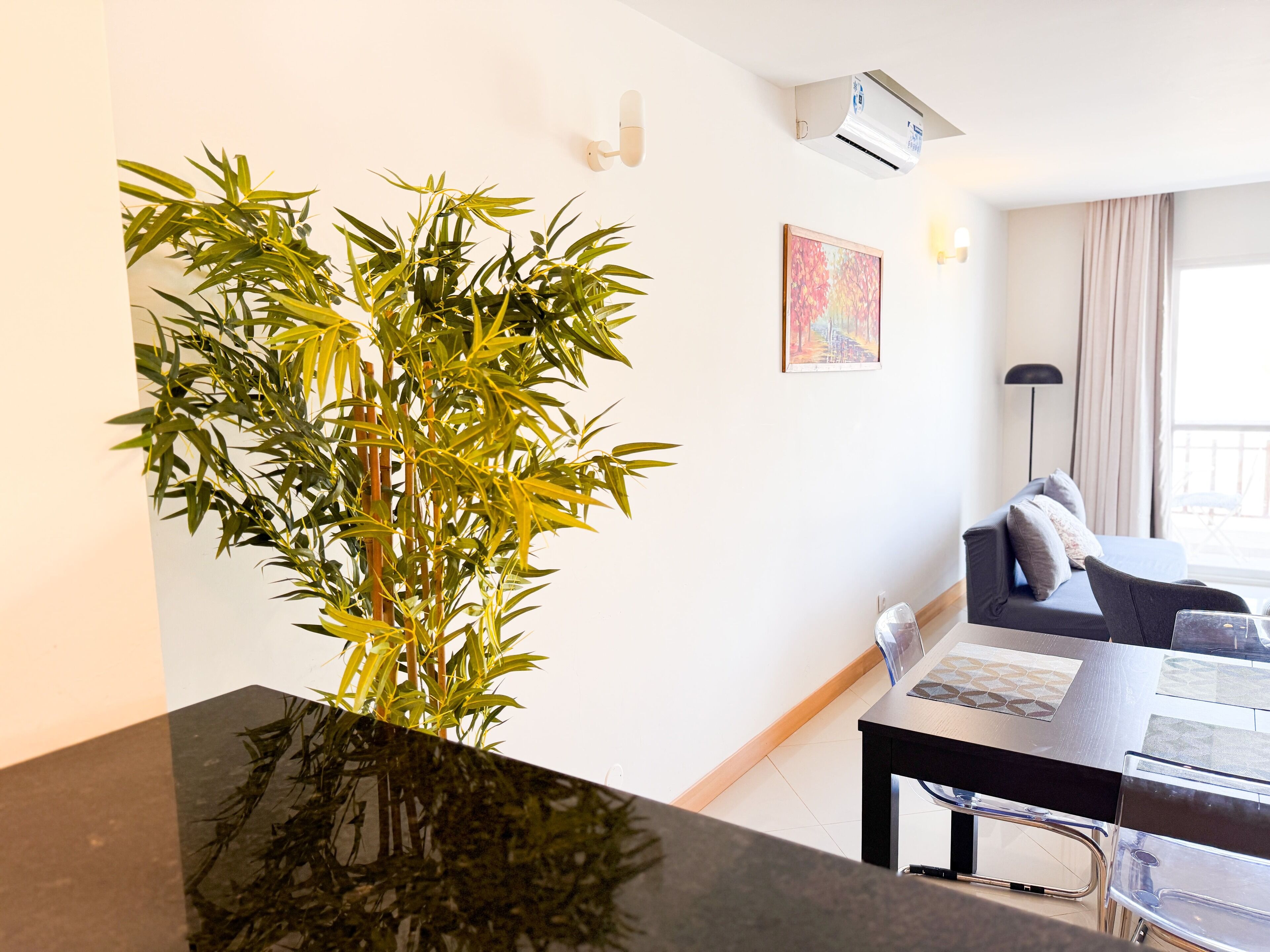 A modern living room with a large bamboo plant, a sofa, a coffee table, and a dining area with chairs.