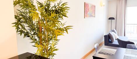 A modern living room with a large bamboo plant, a sofa, a coffee table, and a dining area with chairs.
