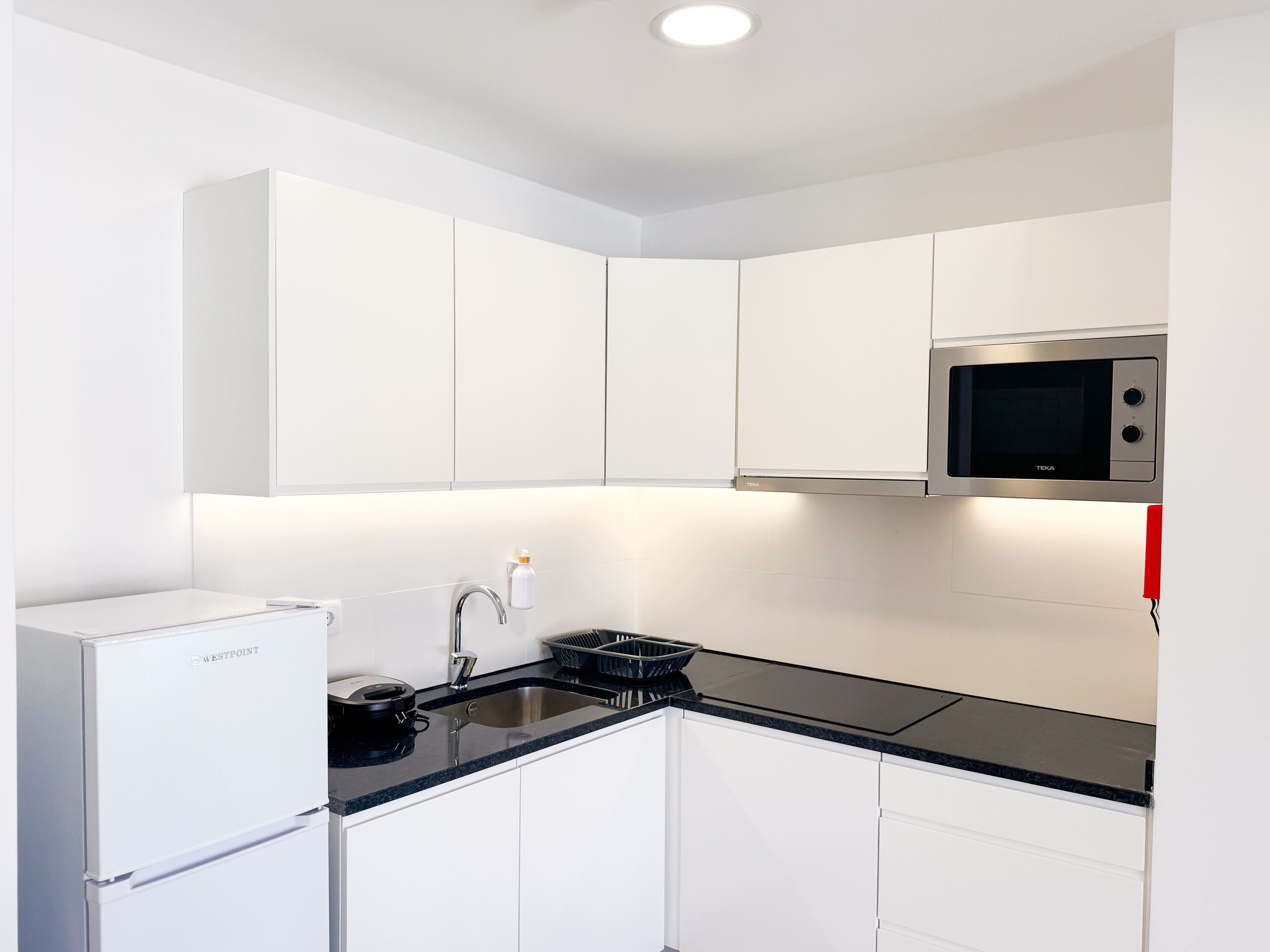 A modern kitchen with white cabinets, a black countertop, a built-in microwave, and a Westpoint refrigerator.