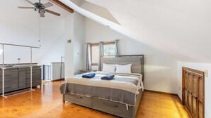 Ein Schlafzimmer mit Bett, Holzboden, Deckenventilator, Kommode und Fenstern.