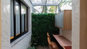 A compact room with a glass wall, a wooden desk, a chair, and a green wall. - Studio Completo Pet-friendly pr Ximo ao Allianz (São Paulo)