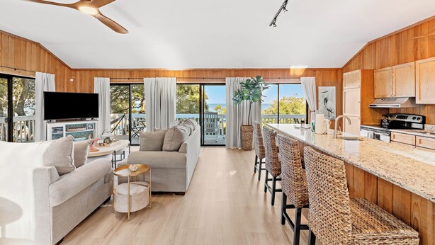A modern kitchen with wooden cabinets, a large island with bar stools, a ceiling fan, and a TV. - Secluded Shoreline Retreat (Saint Helena Island)