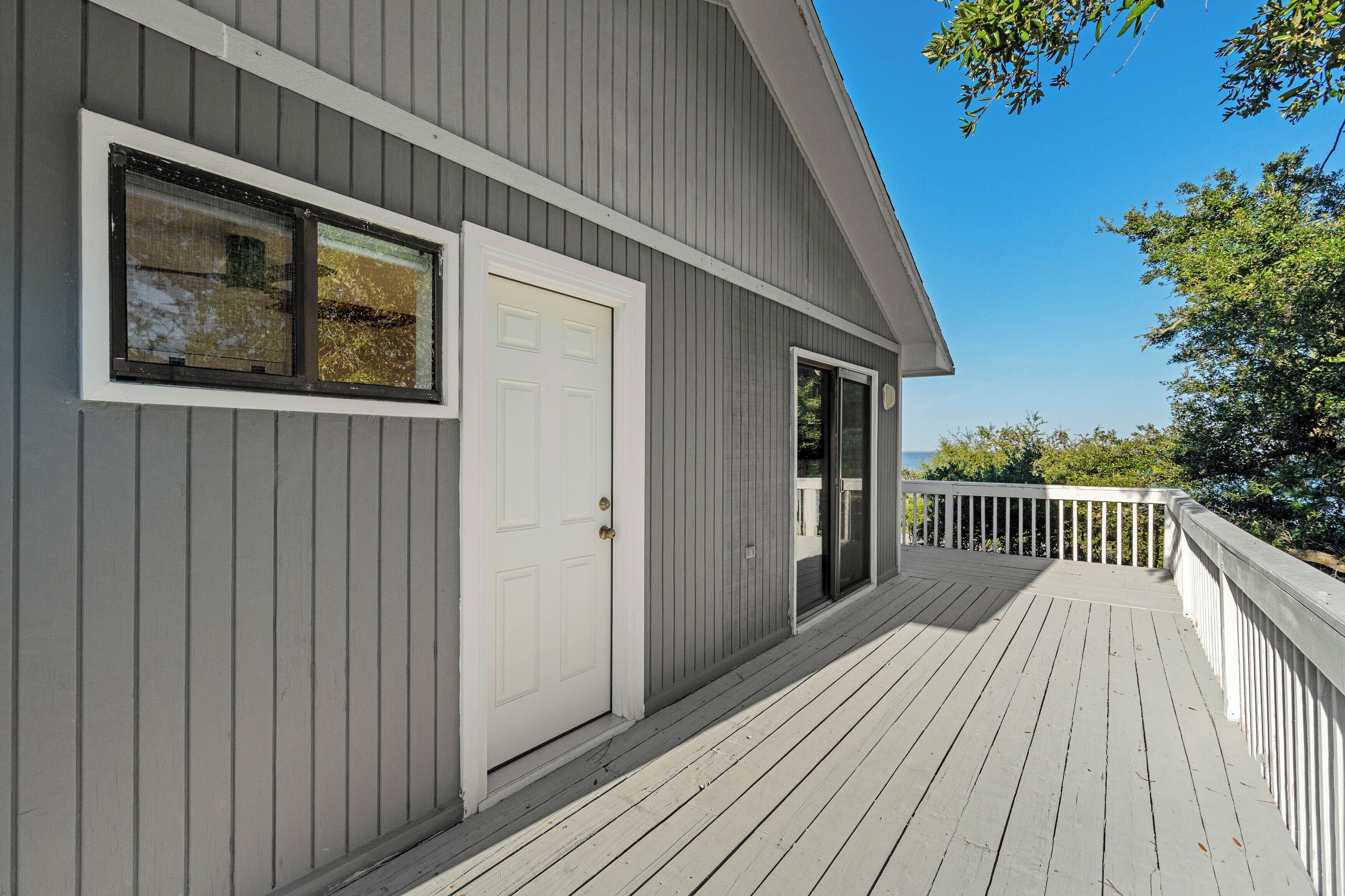 A grey building with a white door and windows, a wooden deck, and a white railing.
