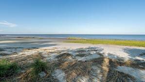 A beach with sand and sparse vegetation, a clear sky, and a calm sea. - Secluded Shoreline Retreat (Saint Helena Island)