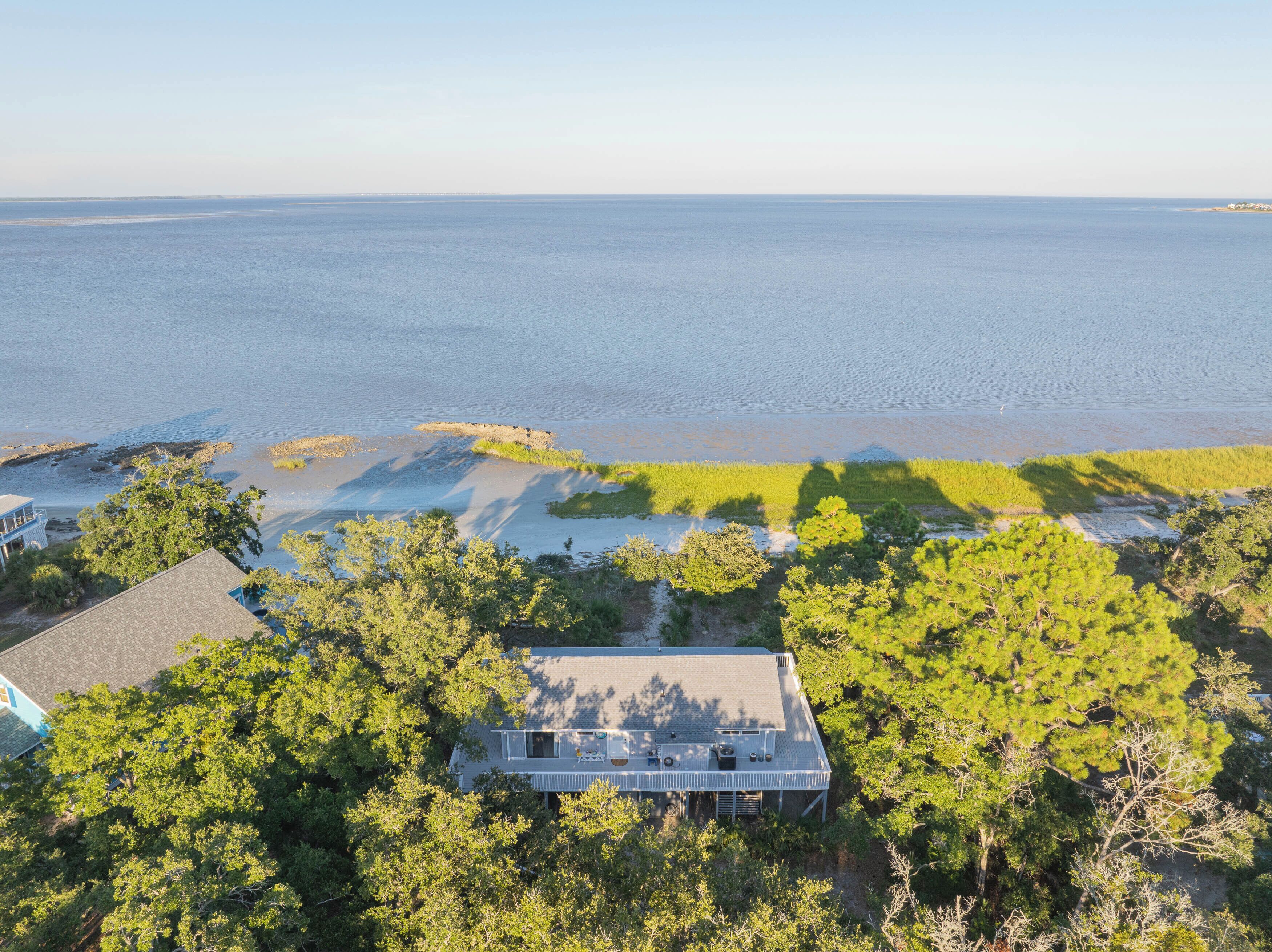 Luchtbeeld van een kustbezit met een groot huis, omringd door dichte bomen, een zandstrand en uitzicht op de oceaan.