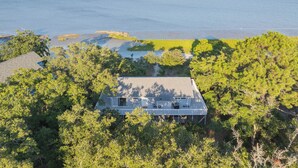 A house with a large deck overlooking a body of water, surrounded by dense trees. - Secluded Shoreline Retreat (Saint Helena Island)