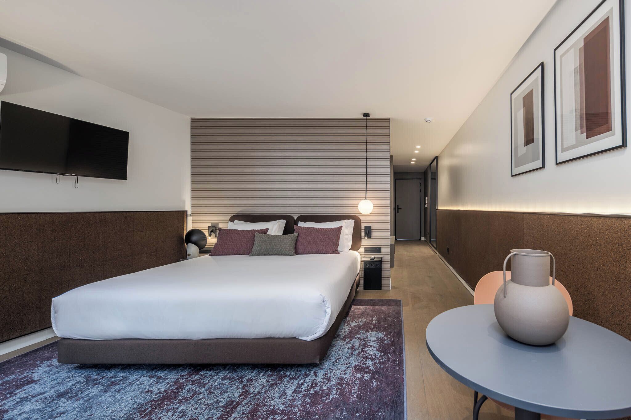 Une chambre d’hôtel moderne dotée d’un grand lit, d’une télévision à écran plat, d’une table de chevet et d’une petite table ronde sur laquelle est posé un vase.