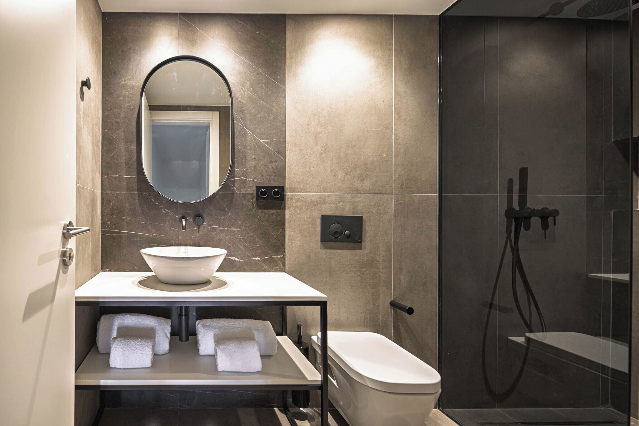 Une salle de bain moderne avec un lavabo blanc, un grand miroir, des toilettes et une douche à parois de verre.