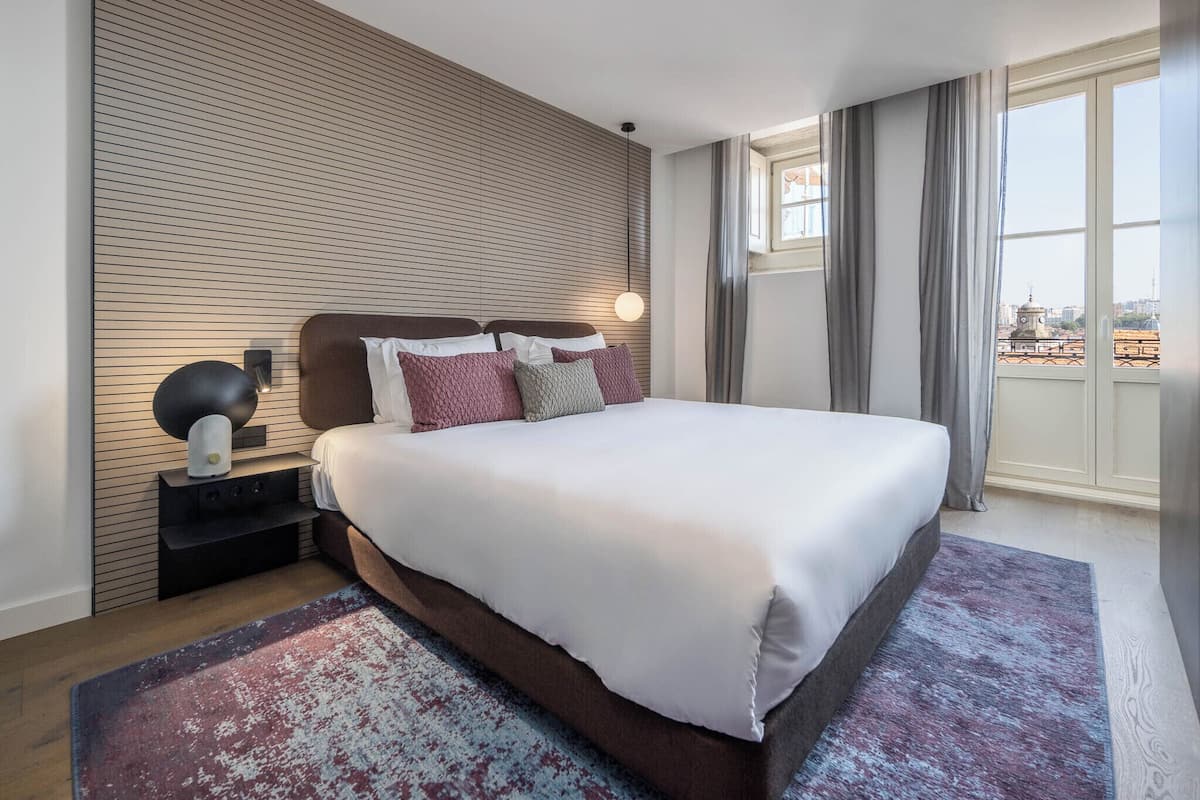 Un hotel moderno con una cama grande, una mesita de noche con lámpara, un panel de pared de madera y vistas a la ciudad a través de la ventana.