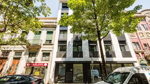 Un immeuble à plusieurs étages doté d’une façade moderne, une devanture de magasin avec une enseigne et une voiture garée.