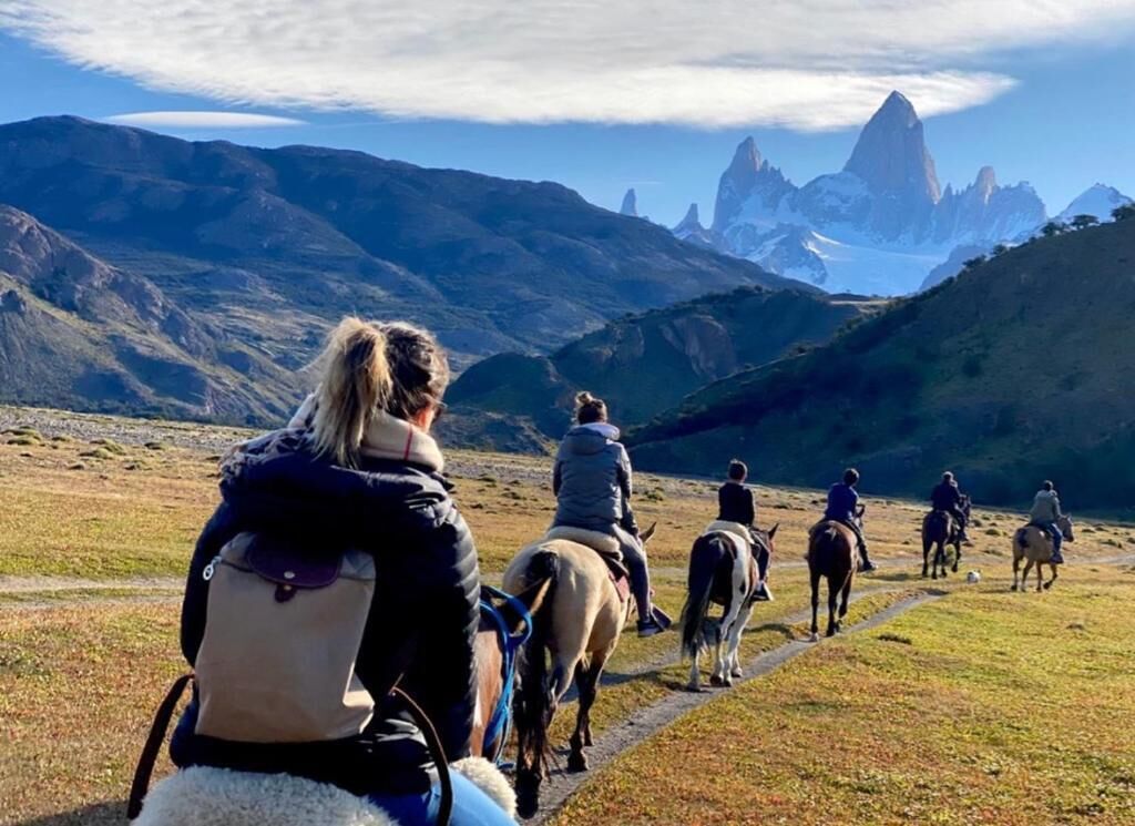 Un grupo de personas montando a caballo por un sendero, con un terreno montañoso al fondo.